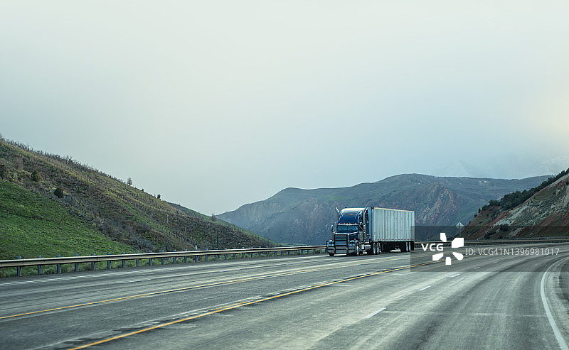 在犹他山脉行驶的蓝白色半挂卡车图片素材