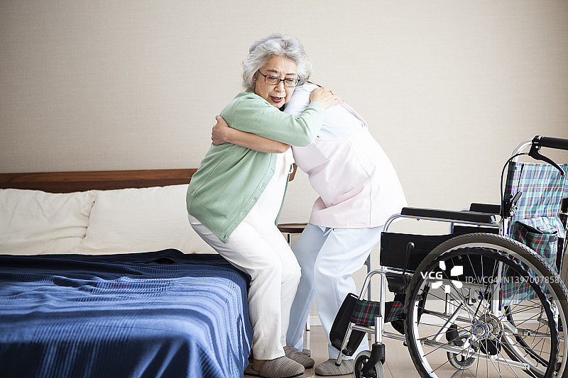 一位年轻的亚洲护理人员正在帮助一位老妇人从床上转移到轮椅上图片素材