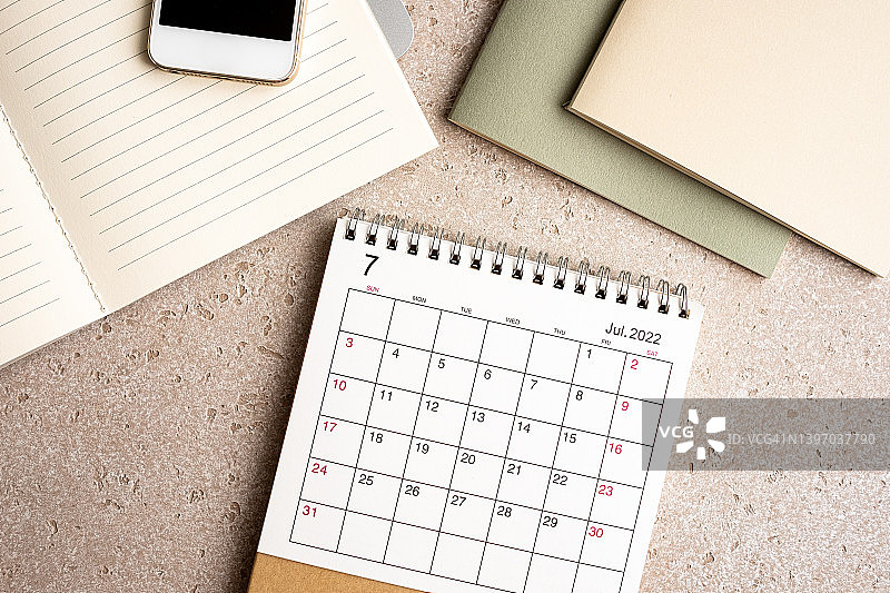 办公桌与文具，包括笔记本电脑、记事本、智能手机和2022年7月台历，混凝土背景，顶视图，带复制空间图片素材
