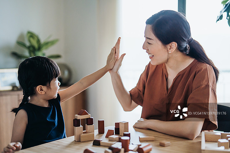 快乐的年轻亚洲母亲和女儿在家一起玩木制积木，击掌欢呼，享受亲子时光图片素材