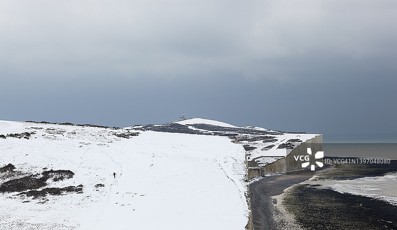 人们沿着白色悬崖走向海边灯塔的冬季雪景图片素材