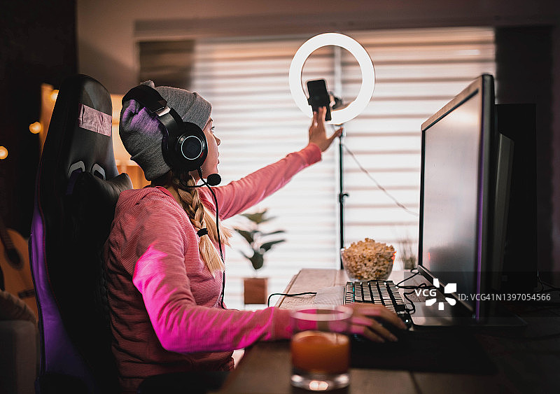 女孩在家玩电子游戏并直播。图片素材