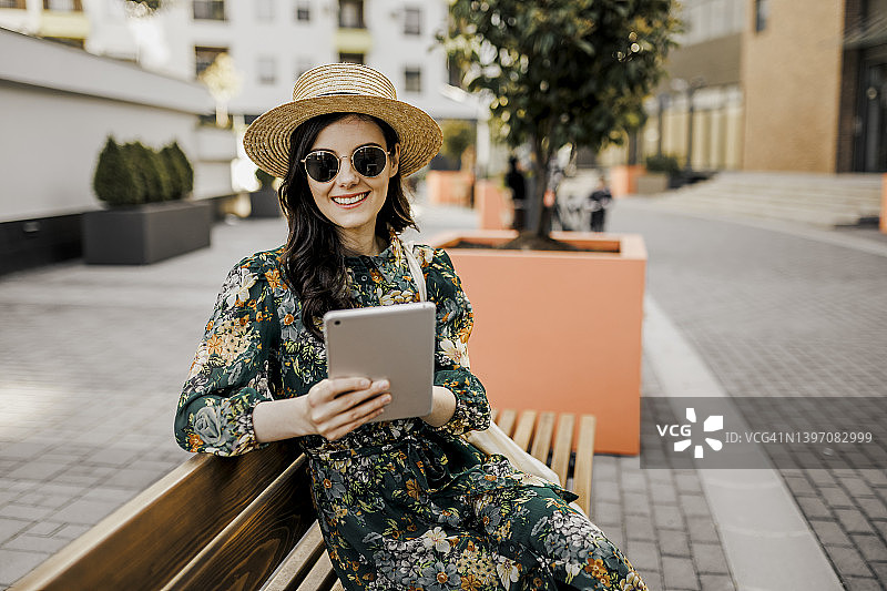 微笑的女人在公园里用平板电脑阅读杂志图片素材