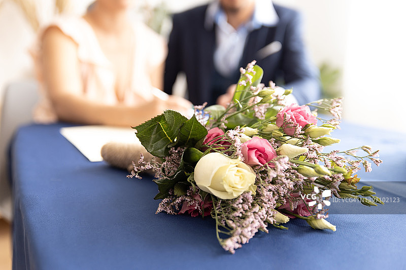 登记处办公桌上的花束和背景中无法辨认的新婚夫妇图片素材