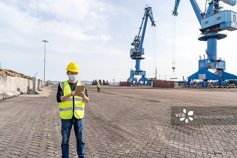 亚洲码头工人于港口吊臂前使用平板电脑图片素材