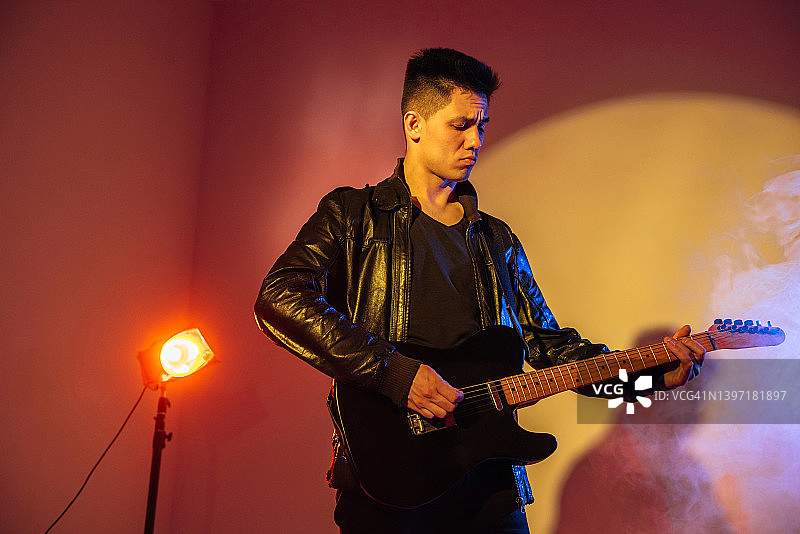 男吉他手在舞台霓虹灯下用吉他演奏音乐图片素材