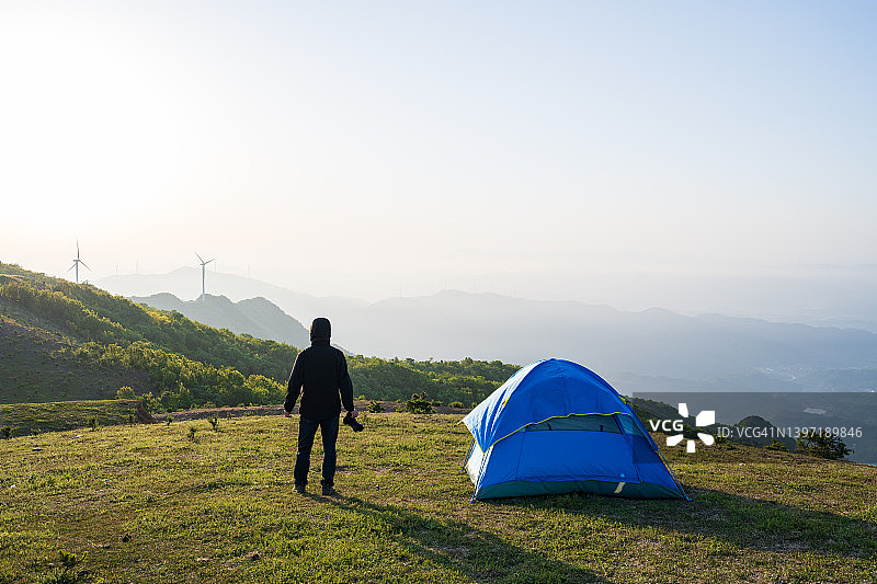 日出时，男子站在露营帐篷旁图片素材