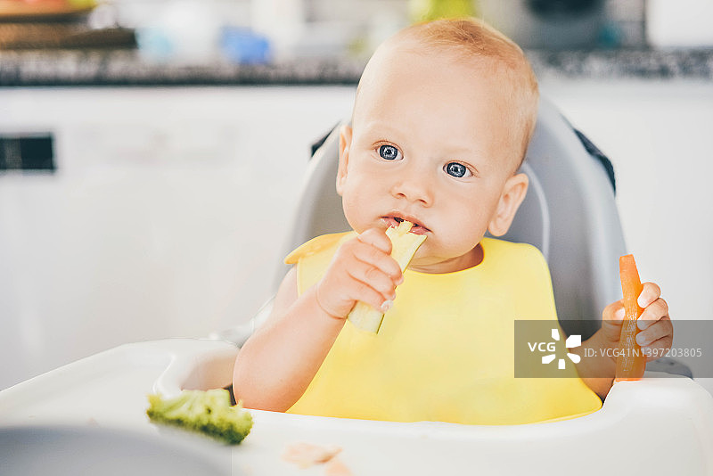 小女孩坐在高脚椅上吃蔬菜。图片素材