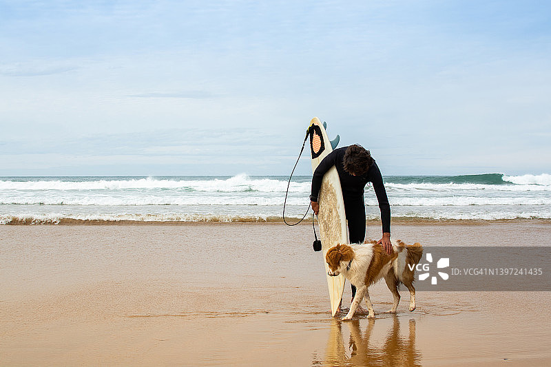 冲浪后在海滩上问候他的狗的男人图片素材