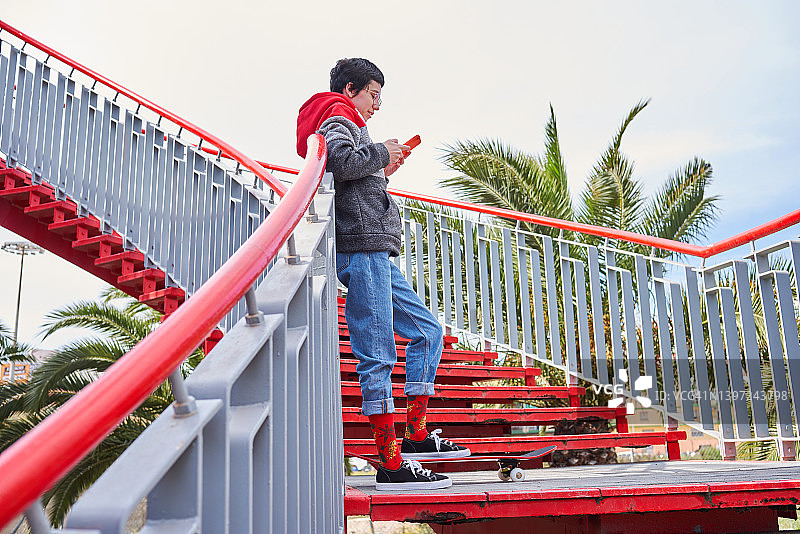在楼梯上使用手机的少女，旁边是她的滑板图片素材
