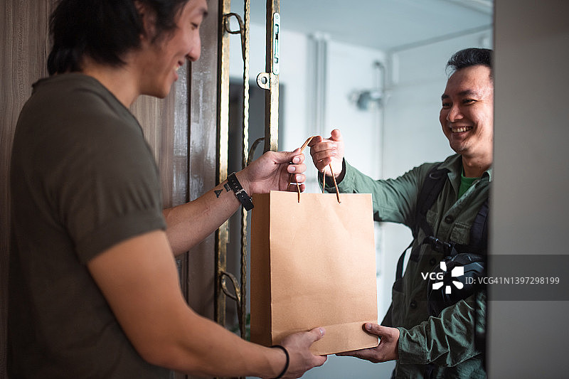 亚洲外卖员将食物送到公寓业主手中图片素材