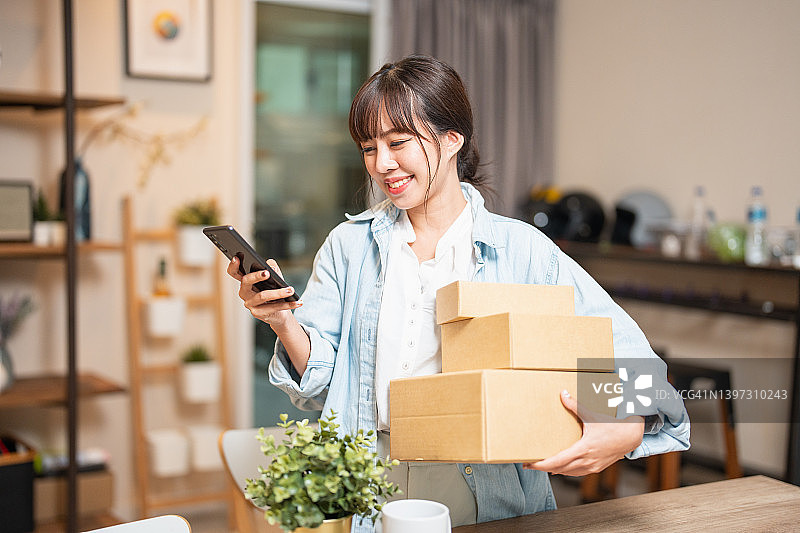 年轻亚洲女性在家使用信用卡和手机/笔记本电脑进行网上购物图片素材