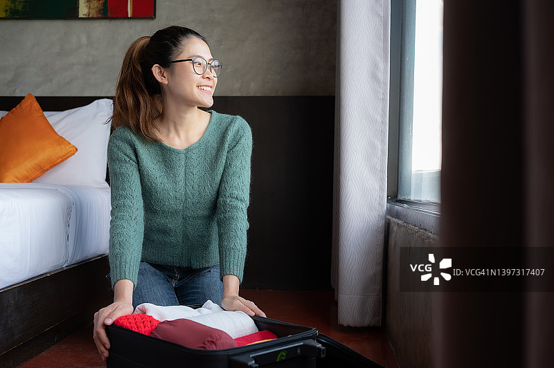 快乐：亚洲女人打开她的手提箱，整理衣服，准备在假期旅行图片素材