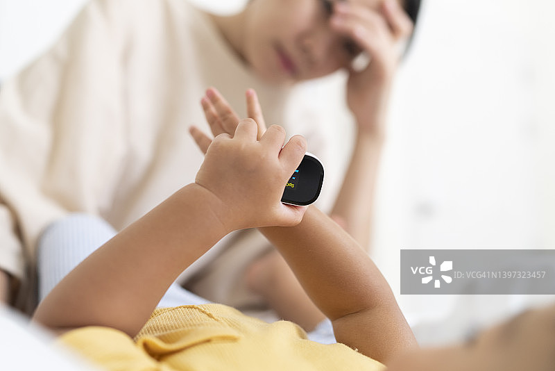 亚洲母亲在家隔离期间使用脉搏血氧仪为女儿检查血氧水平（SpO2）图片素材