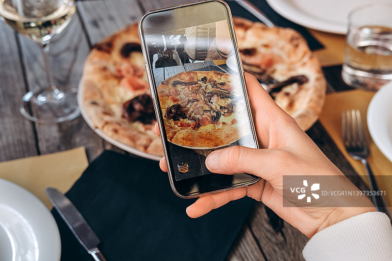 女人用智能手机在意大利餐厅拍摄美味的意大利披萨图片素材