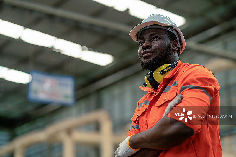 在汽车零件制造生产线上快乐地站立并拿着手臂的保密工程师图片素材