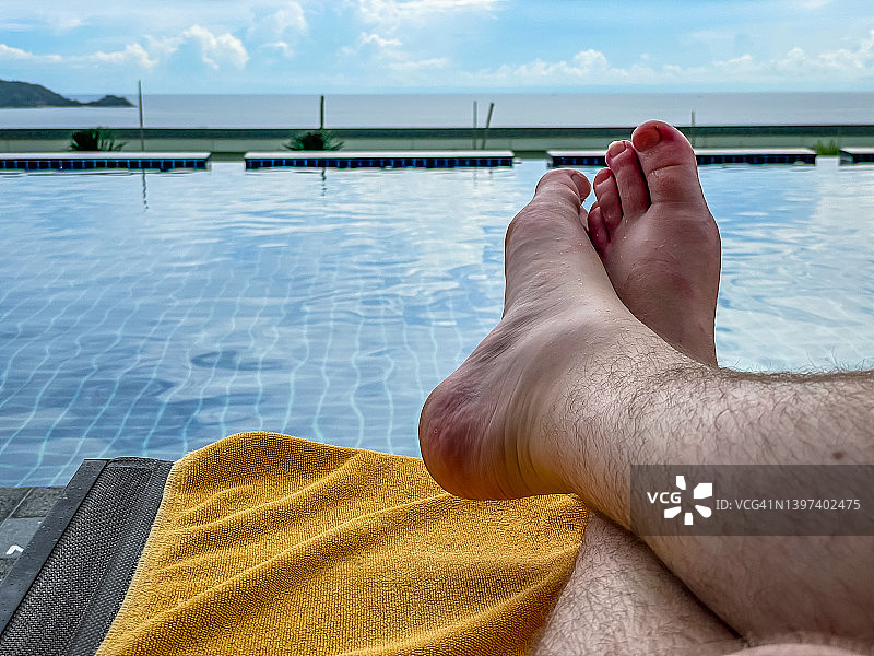 年轻白人男性在热带豪华酒店度假村的阳光下放松，海滩和游泳池边的日光躺椅。健康福祉、休息、自由、假期、度假和旅行的概念图片素材