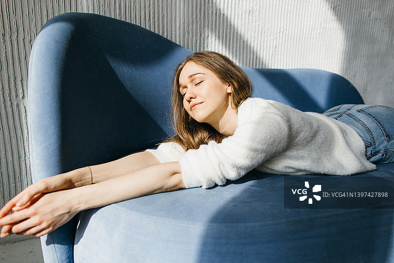 快乐的年轻女人在舒适的沙发上享受阳光图片素材