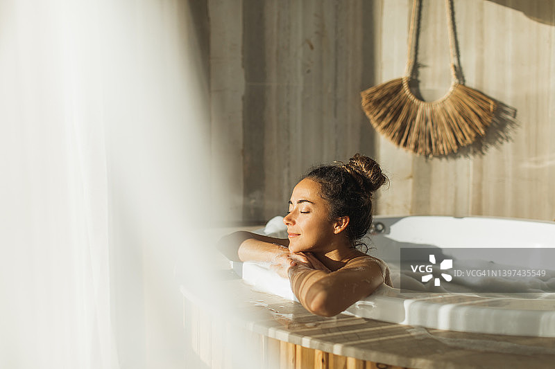 年轻女子在桑拿后享受热水浴缸，在水疗中心休闲放松，巨大的豪华浴缸图片素材