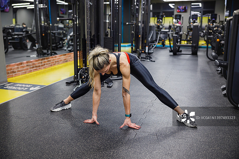 女人在健身房双腿分开站立前屈拉伸图片素材
