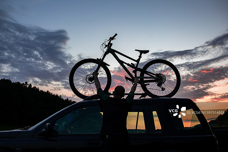 男子在日落时将自行车固定在车顶行李架上图片素材