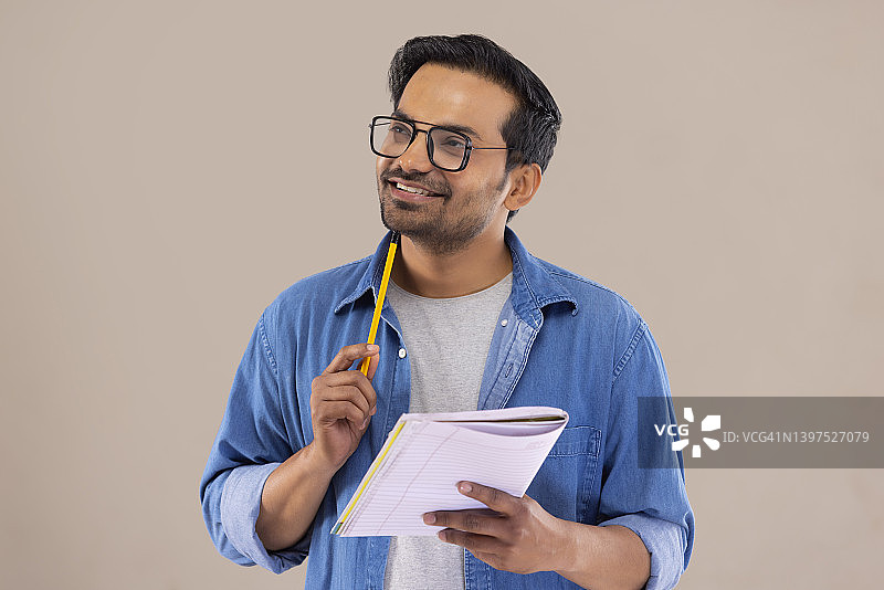 拿着铅笔和笔记本，看向别处思考的年轻男人图片素材