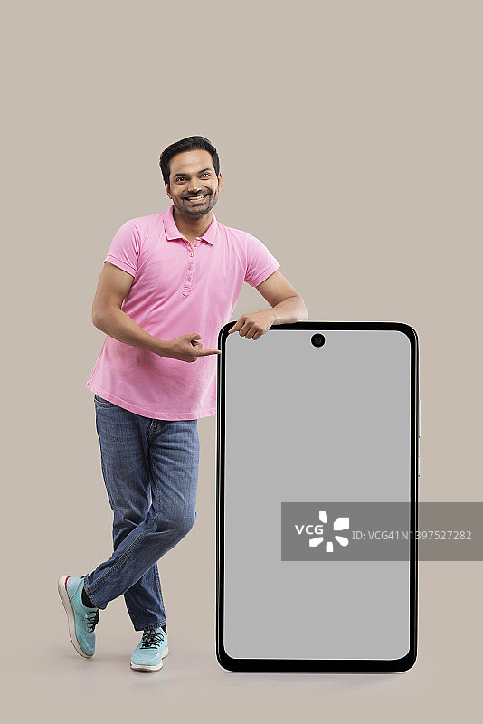 微笑的年轻男人倚靠着大屏智能手机，用手指指点图片素材