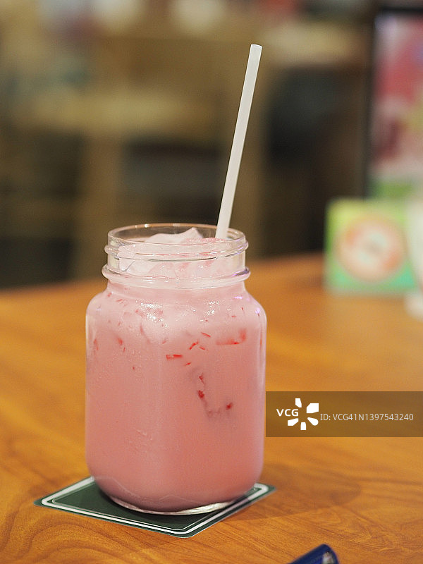 透明玻璃杯装粉色冰牛奶与白色塑料吸管图片素材