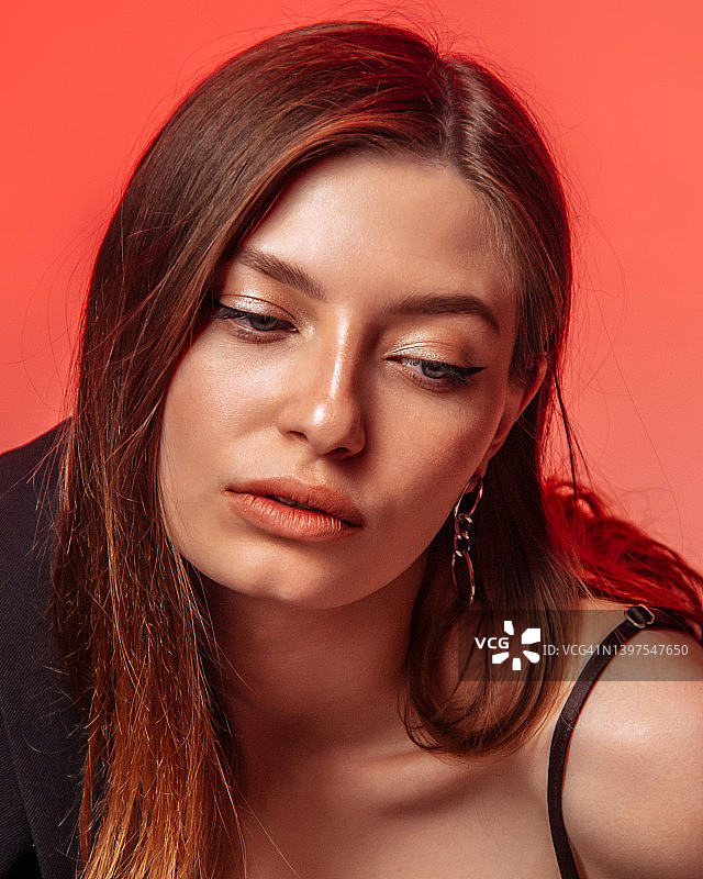 化着精致妆容，在红色背景下摆姿势的自信美丽年轻女人肖像。时尚和美丽。图片素材
