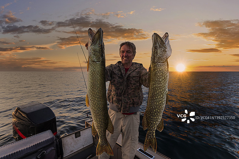 快乐的渔民手持两条大梭鱼图片素材