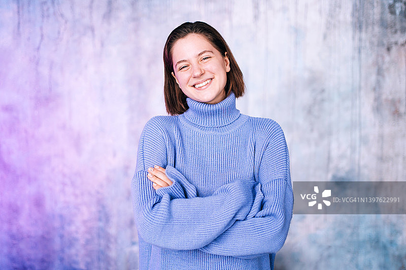 短发灰眼睛的年轻漂亮女人靠在灰色墙壁上，双手交叉，开怀大笑。自然美概念图片素材