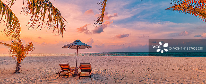 美丽的热带日落风光，棕榈树下的日光浴床和遮阳伞图片素材