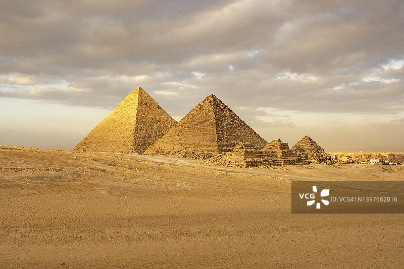 日落时分的吉萨金字塔群，背景是城市风光，埃及开罗图片素材