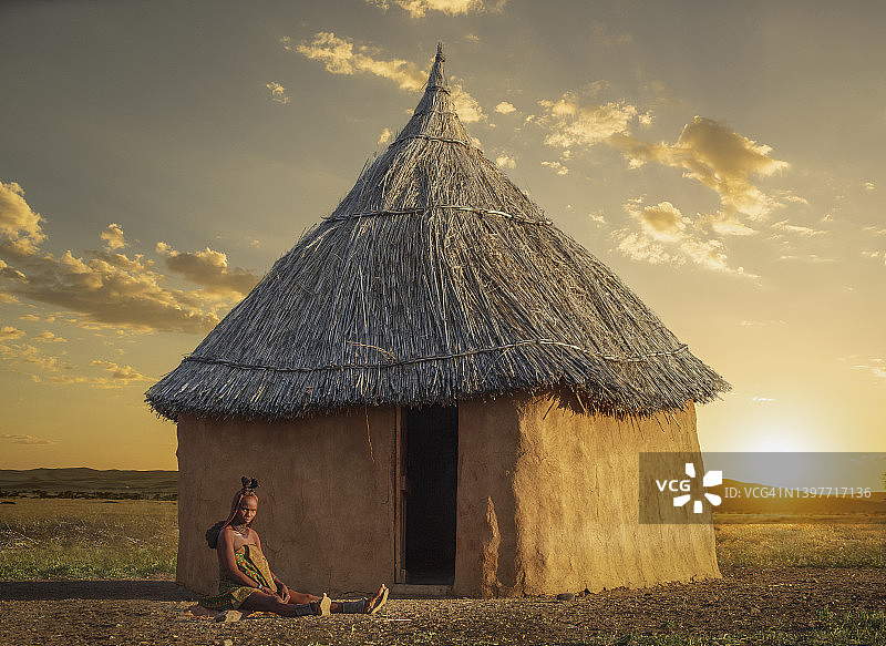 纳米比亚辛巴族妇女坐在日落时分的茅屋旁图片素材
