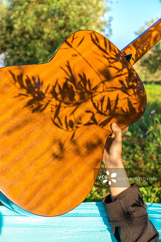 阳光明媚的夏日，树影下抱着原声吉他的人图片素材