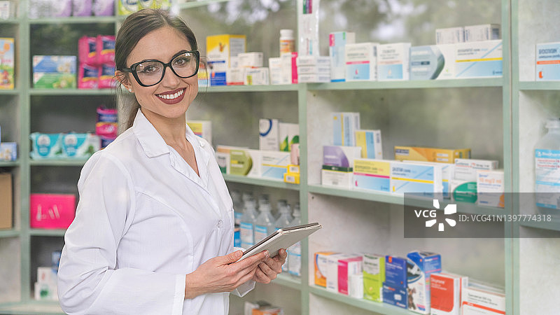 药店里戴眼镜的女药剂师手持平板电脑的肖像图片素材
