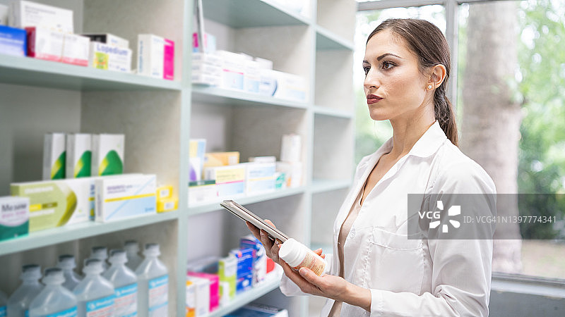 药房：美女药剂师手持平板电脑的肖像；货架上摆满了药品包装。侧面拍摄；整理和包装处方图片素材