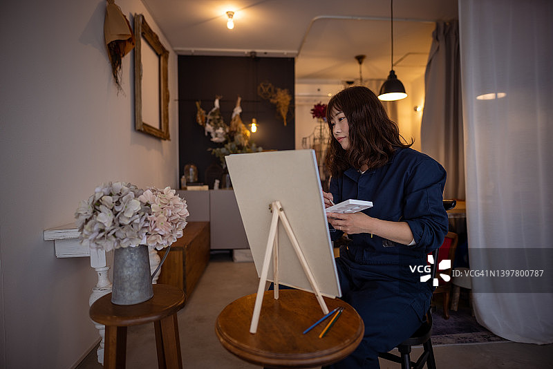 女人在她的工作室里看着绣球花并在画布上绘画图片素材