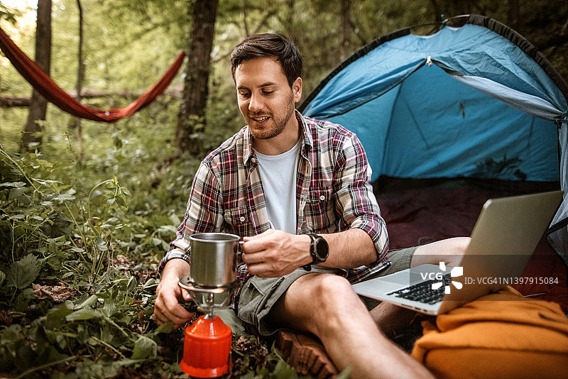 在森林营地用燃气罐炉煮咖啡的年轻男人图片素材