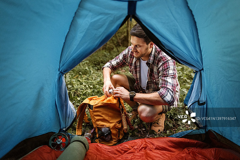 年轻英俊的徒步旅行者在露营帐篷前打开背包图片素材
