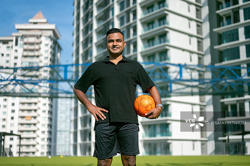 在球场上微笑的亚洲男子足球运动员的户外运动肖像图片素材