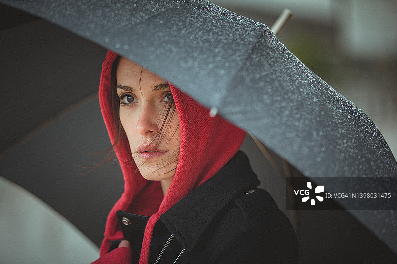 寒冷、多风、下雨天，年轻女子在雨伞下的肖像照图片素材