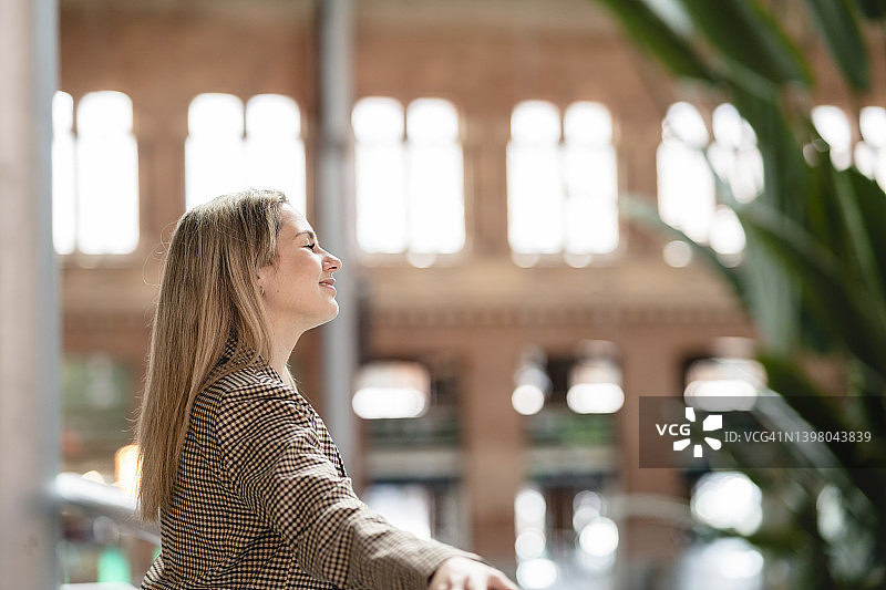 夕阳下，倚窗放松的金发女人图片素材