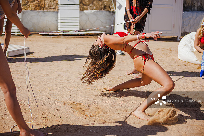 在沙滩上挑战 Limbo 舞的年轻比基尼女子图片素材