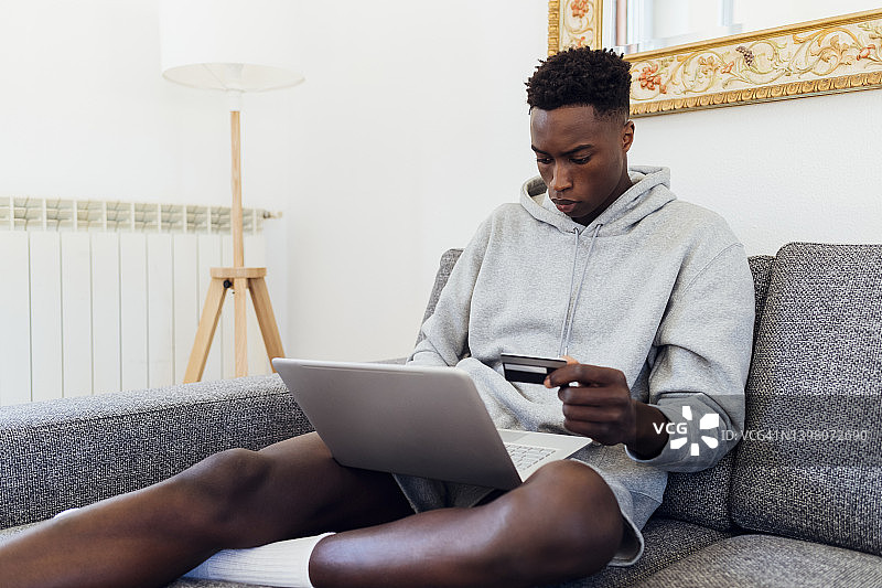 在家中使用笔记本电脑和信用卡的青年人像图片素材