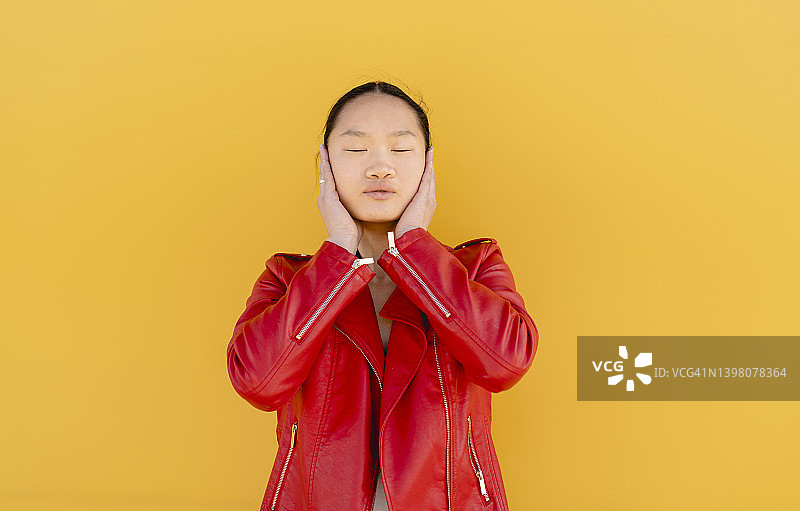 在黄色背景下，用手捂住耳朵的年轻女人图片素材