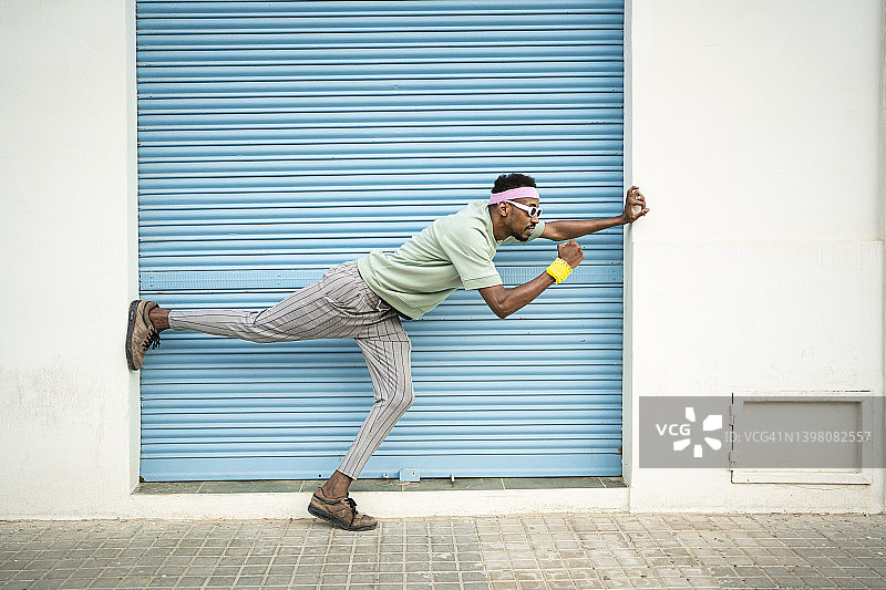 在蓝色百叶窗前单腿站立的嬉戏的年轻人图片素材