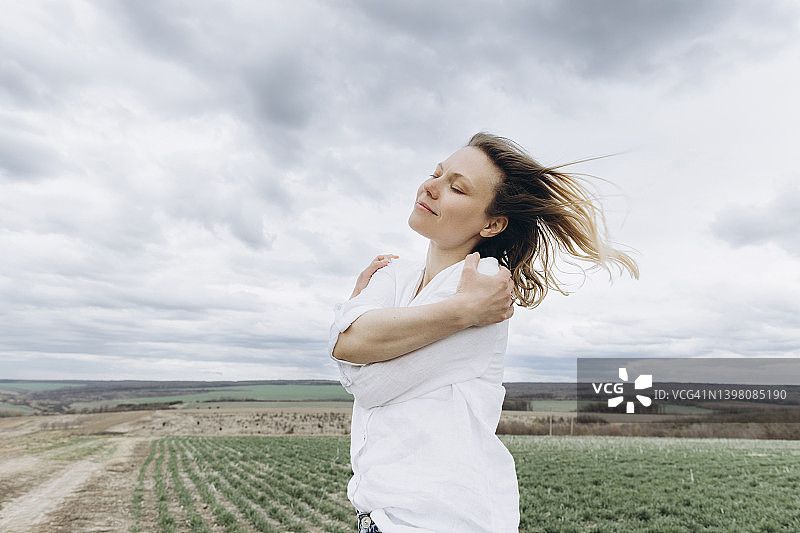 闭着眼睛的女人在农田里拥抱自己图片素材