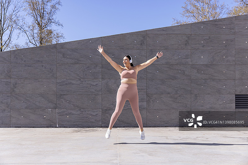 体型丰满的女人戴着无线耳机在人行道上听音乐锻炼图片素材