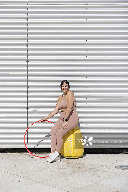 坐在瓦楞墙前，手持塑料圈的微笑女人图片素材